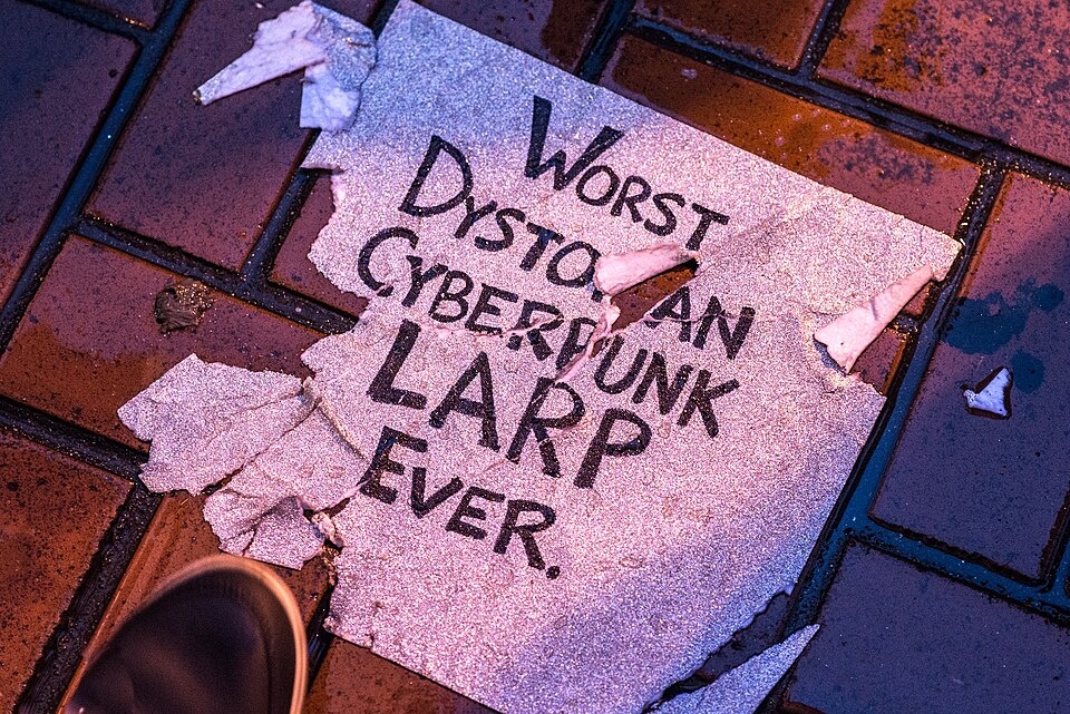 Glittery silver sign, torn and on the ground, with the text "Worst dystopian cyberpunk LARP ever". Cyberpunk, January 21, 2017.