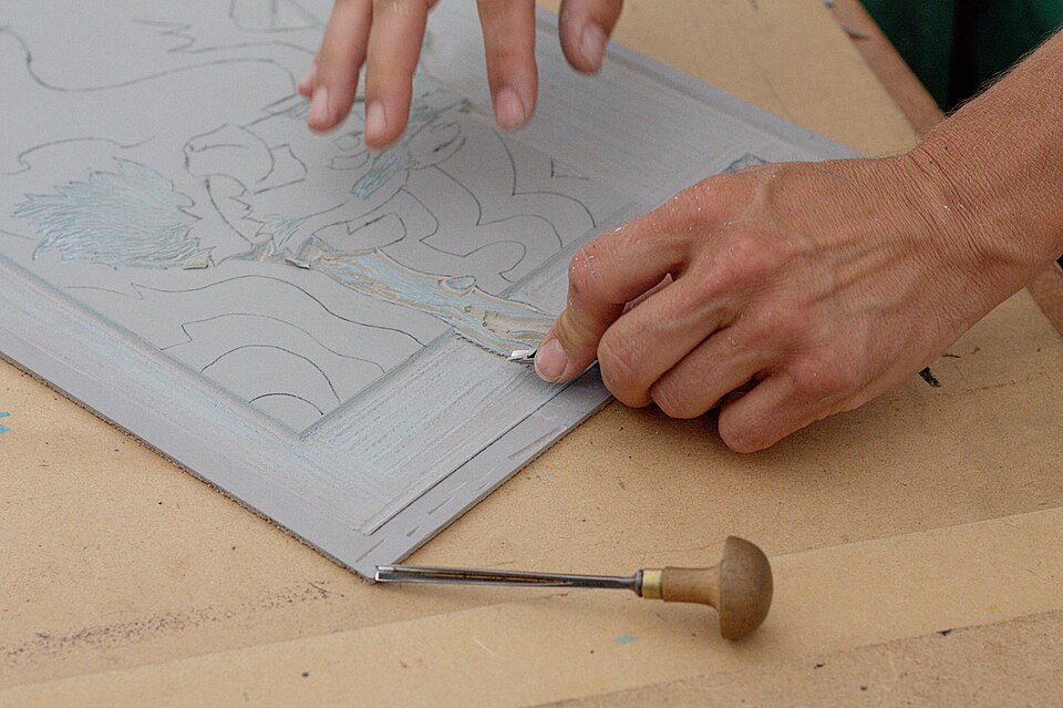 Using a handheld gouger to cut a design into linoleum for a linocut print.